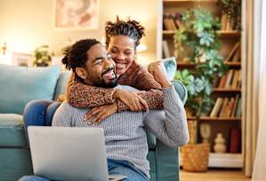 A man and woman are sitting on a couch with a laptop in front of them.