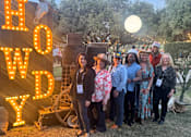 Thumbnail 13 of 21 - A group of people are standing in front of a sign that says "HOW DY".