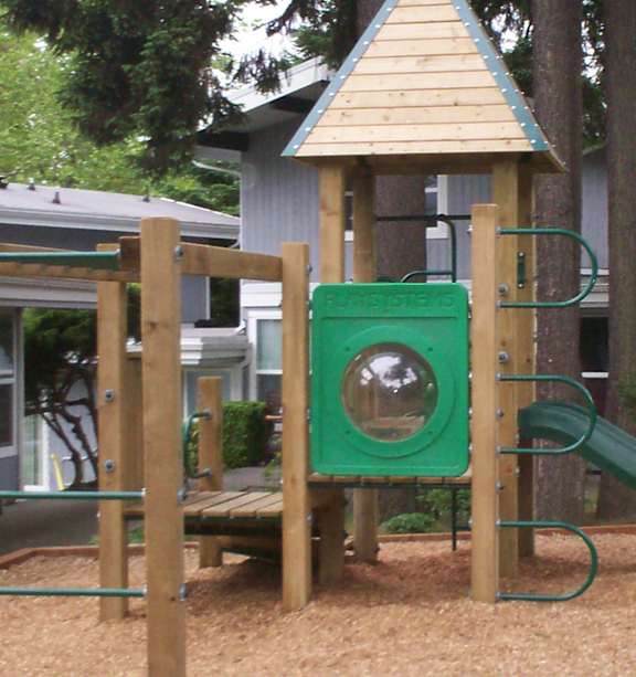 A playground with a green slide and a wooden structure.