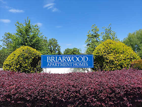 A sign for Briarwood Apartment Homes is in front of some bushes.
