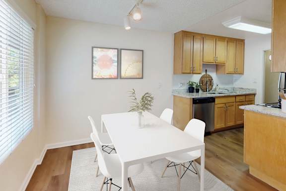 A white dining table with four chairs is in a kitchen with wooden cabinets.
