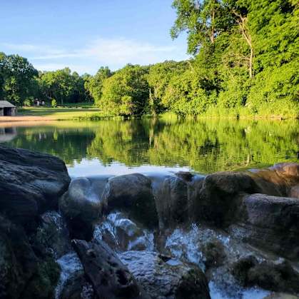 A serene lake with a stone wall in the foreground and a building in the distance.