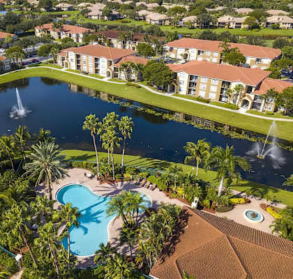 A large swimming pool surrounded by palm trees and a fountain in the middle.
