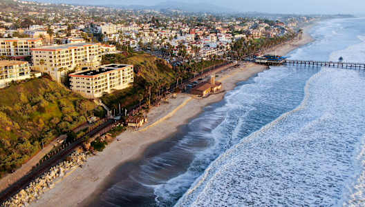 A beach with waves crashing on the shore and buildings in the background.
