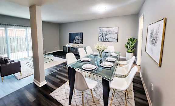 A dining room with a glass table and white chairs.