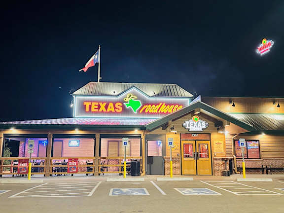 A Texas Roadhouse restaurant at night with its neon sign lit up.