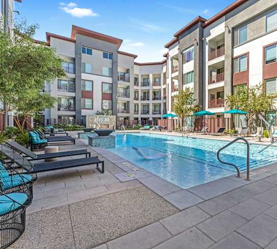 A pool surrounded by apartment buildings and lounge chairs.