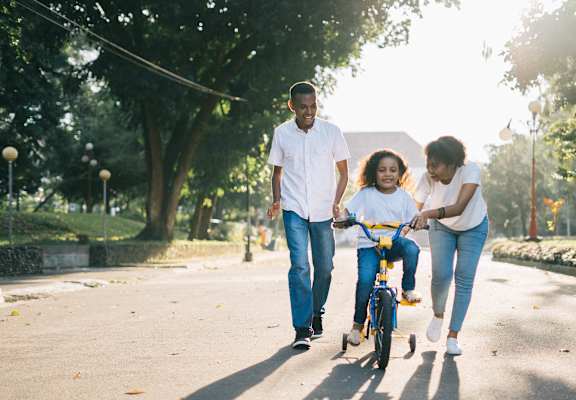 A family of three is walking together in a park with a child on a bicycle.