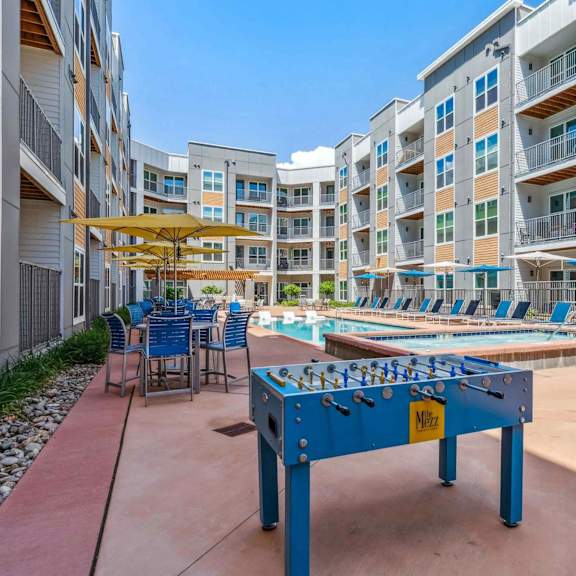 A blue foosball table is in the middle of a courtyard with chairs and umbrellas.