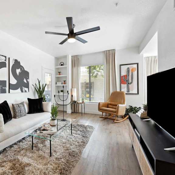 A modern living room with a white sofa, a glass coffee table, and a wooden rocking chair.