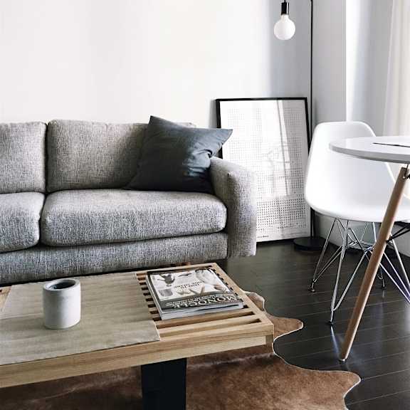 A grey couch with a white chair and a coffee table with a book and a cup on it.
