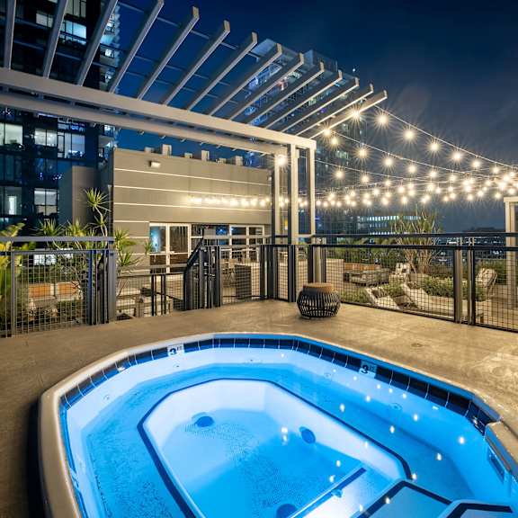 A hot tub sits on a patio with lights strung above it.