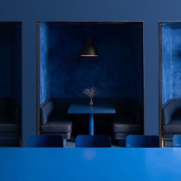 A blue table with chairs and a plant in the middle of a room with blue walls.