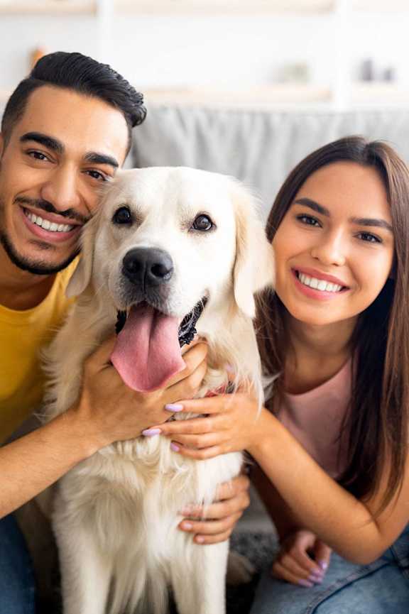 A man and woman are sitting on a couch with a white dog.