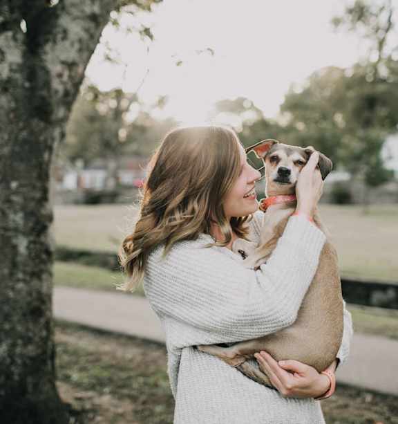 A woman in a white sweater is holding a dog in her arms.
