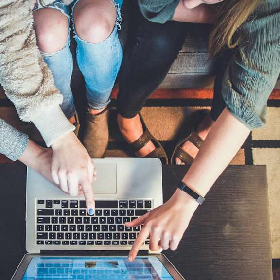 Two people are sitting on a bench with a laptop.