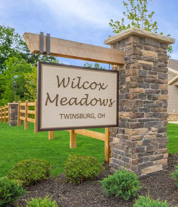 A sign that says "Wilcox Meadows" in front of a stone pillar.