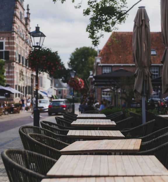 A row of empty tables with wooden tops are set up outside a building.