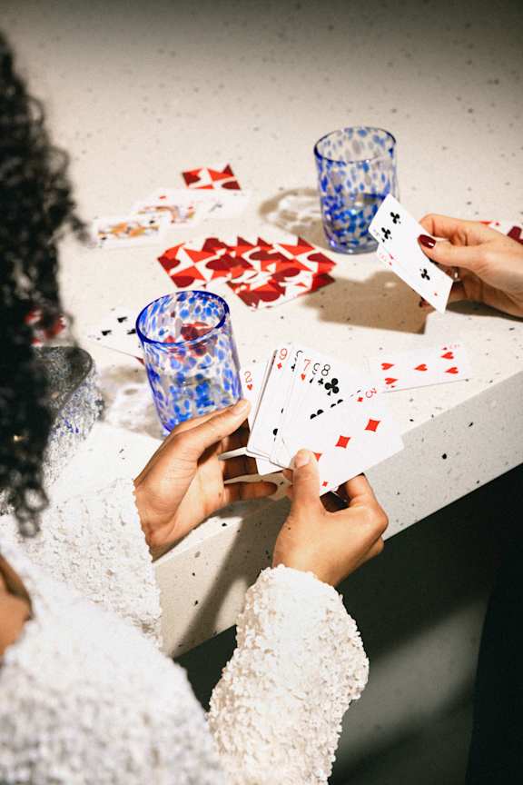 Two people playing cards with a blue glass in the middle.