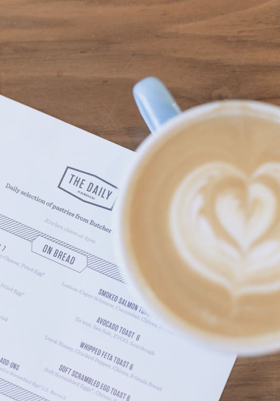 View of a latte with foam art and The Daily menu at The Merchant in South Carolina 29403