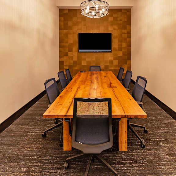 A conference room with a long wooden table, a TV, a chandelier, and chairs at the Park Apartment Homes. 