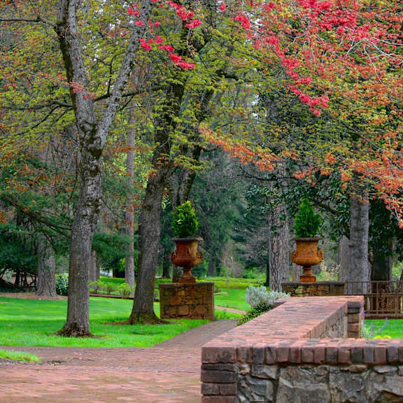 A pathway with a stone wall and two urns on top of it.