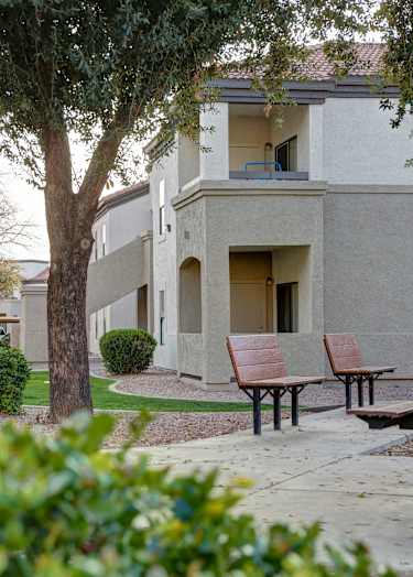 A basketball court with a bench on the side and two houses in the background.