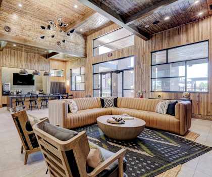 The amazing resident lounge with couches, decorations, large windows, unique overhead lighting, plush chairs, and coffee tables at and a community kitchen with a coffee station, bar counter with stools, and TV at the Encore Apartments. 