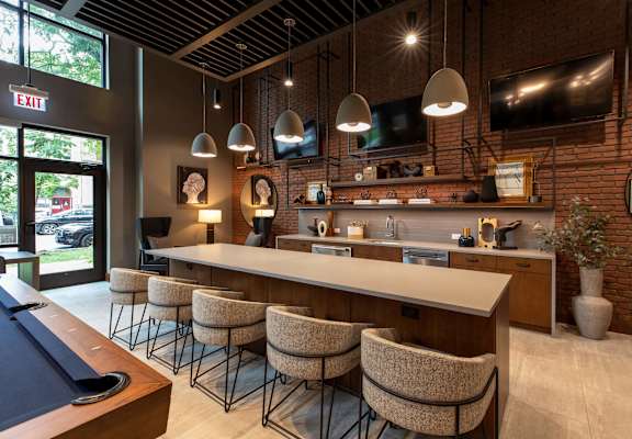A pool table is in the middle of a room with a bar and chairs.
