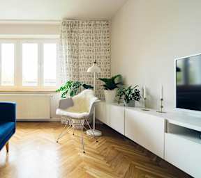 A blue sofa sits in a living room with a white chair and a television.