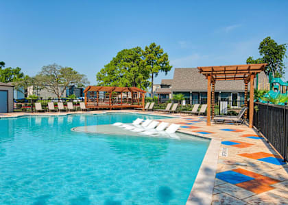 A pool with a wooden pergola and lounge chairs.