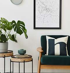 A living room with a green chair, a potted plant, and a framed map on the wall.