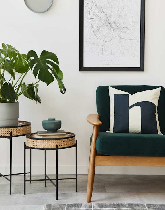 A living room with a green chair, a potted plant, and a framed map on the wall.