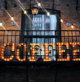 An industrial Coffee sign that lights up against a brick building.