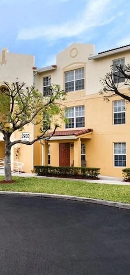 well-kept apartment building exterior with towering trees and lush landscaping