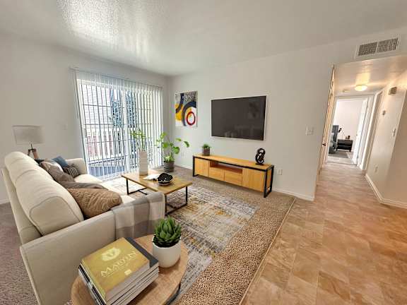 Bridgeside Landing Apartments in Taylorsville, Utah, Living area with tan couch, flatscreen television on wall, balcony off the room, hallway back to bedroom.