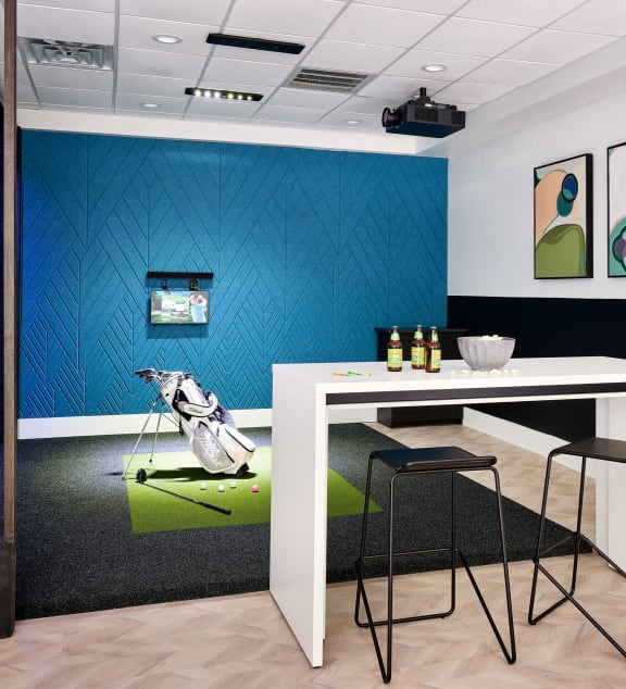 a room with a table and chairs in front of a golf simulator