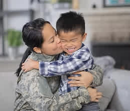 A woman in military uniform hugs a young boy.