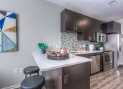 Thumbnail 64 of 78 - a kitchen with dark cabinets and a white counter top with two stools in front of it  at EdgeWater at City Center, Lenexa