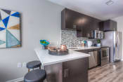 Thumbnail 64 of 78 - a kitchen with dark cabinets and a white counter top with two stools in front of it  at EdgeWater at City Center, Lenexa
