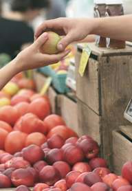 A person is handing a red apple to another person at a fruit stand.