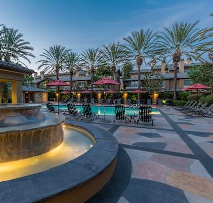 a fountain in the middle of a courtyard with a building and palm trees in the background at St. Moritz Apartments,Aliso Viejo