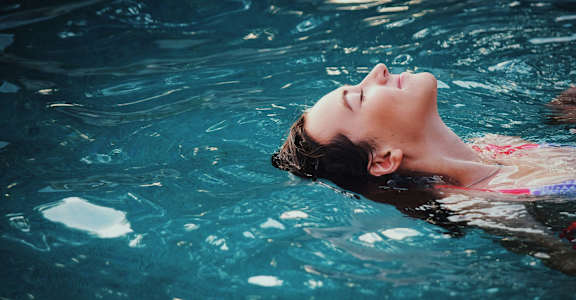 A person is floating in a pool with their eyes closed.