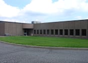 Thumbnail 1 of 3 - A large grey building with a green lawn in front.