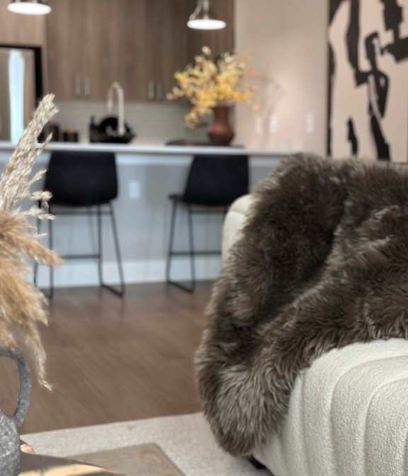 A grey fluffy couch with a white cushion is in the foreground of a modern kitchen at The Beacon at 331 Apartments, Santa Rosa Beach, Florida
