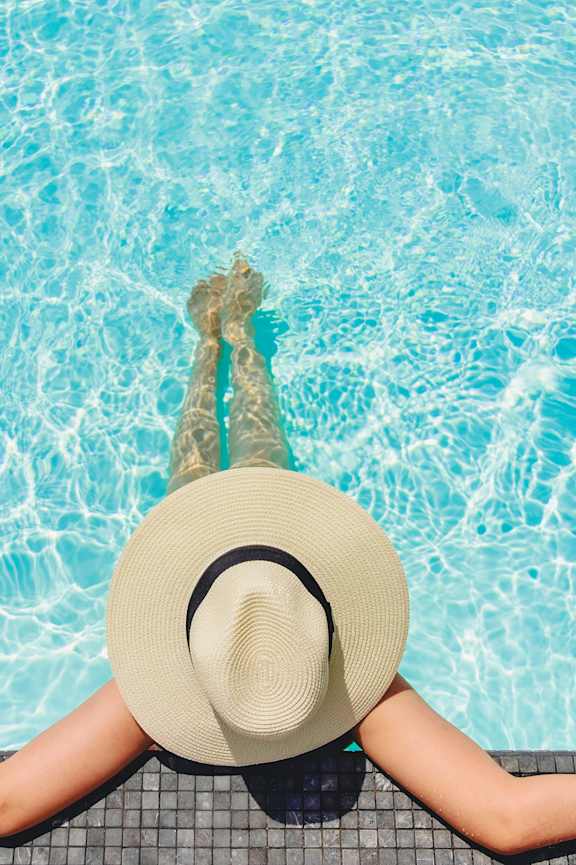 A woman in a hat is relaxing by the pool.