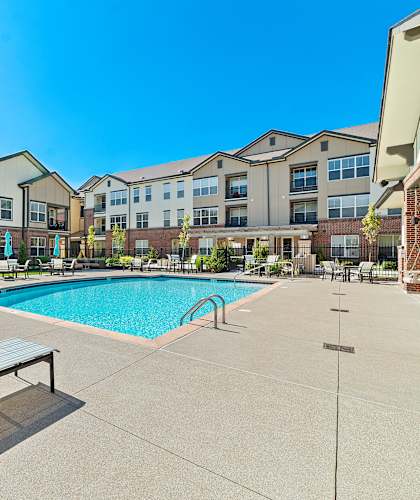 A swimming pool surrounded by sun loungers in front of apartment buildings.