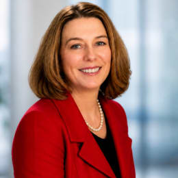 a woman wearing a white jacket and a purple shirt and a pearl necklace