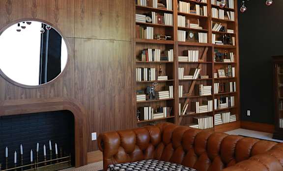 A living room with a fireplace, a round leather sofa, and a bookshelf filled with books.