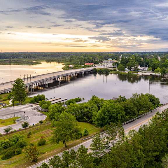 A serene landscape with a pier extending into a lake, surrounded by lush greenery and a clear sky.